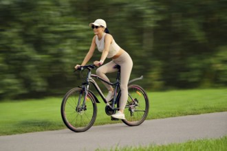 A slender woman in a tank top, cap and leggings quickly rides on a bicycle along the alley in a