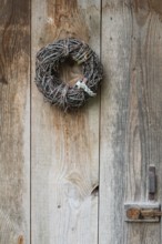Door wreath made of natural materials in front of an old wooden door, North Rhine-Westphalia,