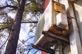 An old and rusty air conditioner hanging on the hotel building, in the sunny outdoor, seaside