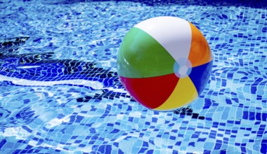 Colorful beach ball floats on the surface of a pool reflecting sunlight on a summer day