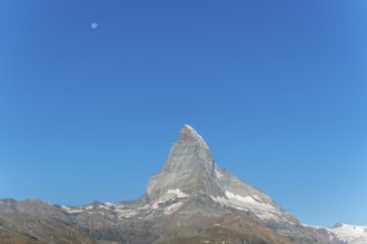 The iconic Matterhorn stands high above a clear evening sky illuminated by a bright moon. This