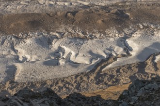Detailed glacier formations stretch across the rocky landscape, revealing crevasses and structures,