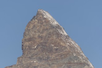 A towering Matterhorn mountain peak stands prominently against the clear blue sky, revealing rocky