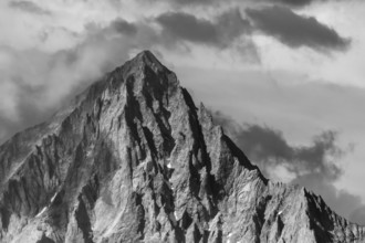 An impressive mountain peak stands in the clouds and reflects the last rays of sunlight until dusk.