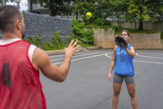 Two baseball players practicing catching on a court, with a woman wearing a glove attempting to