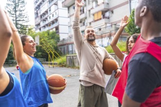 Basketball coach holding a ball under his arm and raising his hand while explaining game strategy