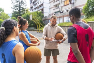 Basketball coach holding a ball and taking notes on a clipboard while engaging with team players on