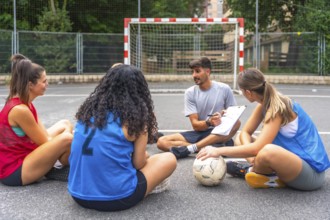 Soccer coach sitting on the ground with clipboard explaining game strategy to female players