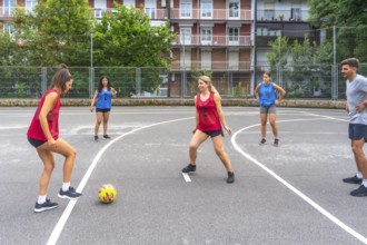 Female soccer players in red and blue jerseys kicking a yellow soccer ball during a friendly