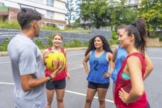 Male coach holding a soccer ball, engaging in conversation with a group of female soccer players