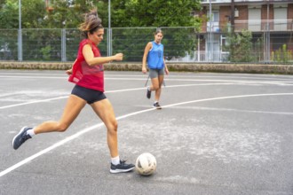 Two women athletes playing soccer on an outdoor court are passing the ball to each other,