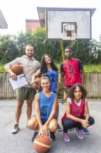 Multi ethnic basketball team posing with their coach on an outdoor court, showcasing teamwork,