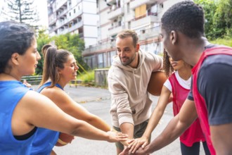 Smiling basketball players joining hands in a huddle before a street match, showcasing teamwork and
