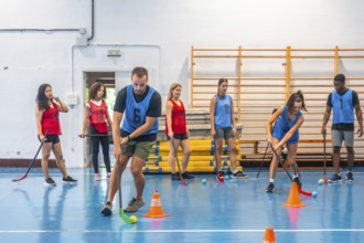 Floorball players practicing drills on court with coach watching, focusing on stick handling skills