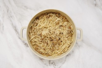 Overhead view of double handled pot with cooked noodles and creamy mushroom sauce on a marble