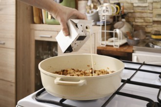 A hand pours cream over roasted mushrooms in a pot on the stove