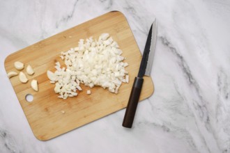 Diced onions and whole garlic cloves rest on a wooden cutting board beside a sharp knife. The