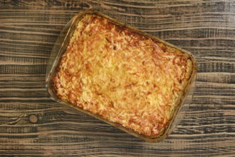 A delicious loaded baked potato casserole sits in a glass dish on a rustic wooden table. The