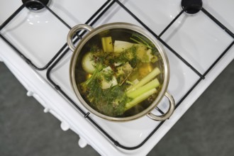 A pot with fresh vegetables boiling on a stove in a contemporary kitchen. Ingredients include