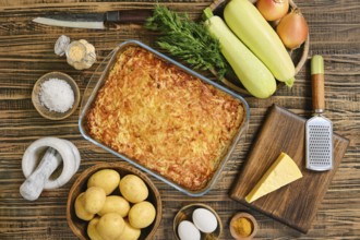 Loaded baked potato casserole sits in a glass dish surrounded by fresh vegetables and spices.