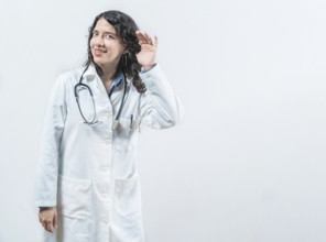 Latin female doctor listening to gossip, looking at camera. Doctor with hand on ear listening to