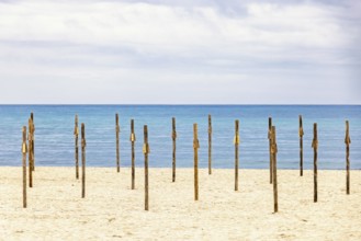 Parasol poles on a empty sandy beach by the Mediterranean sea with a seascape view to the horizon,