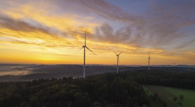 Wind turbines above a rich forest landscape at sunrise with a yellow pastel sky, near Schorndorf,