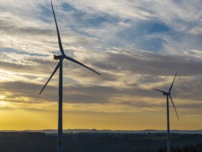 Two wind turbines turn under the early, dramatically lit clouds of a new day, near Schorndorf,