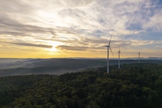 A row of wind turbines overlook a wooded area as the morning fog lifts, near Schorndorf, Rems-Murr
