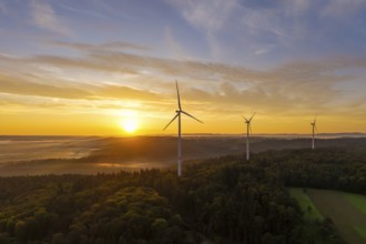 Three wind turbines at sunrise with a golden sky over a forest landscape, near Schorndorf,