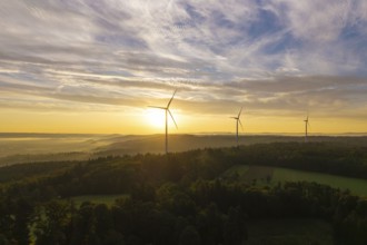 Three wind turbines above a hilly landscape, morning clouds reflecting the rising sunlight, near