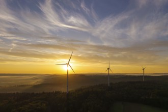 Wind turbines rise in front of a sunrise over a green landscape, creating a tranquil atmosphere,