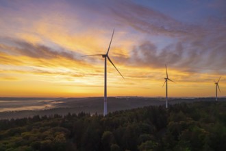 Wind turbines on a hill, dramatic sky colours at sunrise over a forest landscape, near Schorndorf,