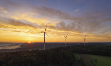 Three wind turbines at sunrise over a misty and golden landscape, near Schorndorf, Remstal,