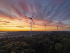 Wind turbines in the foreground of an intense pink-orange sunrise over a forest, near Schorndorf,