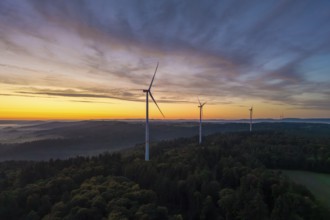 Three wind turbines on a wooded hill with a dramatic sunrise sky, near Schorndorf, Remstal,