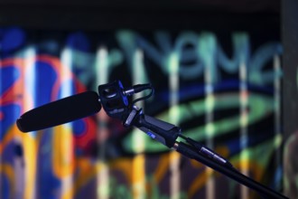 A microphone in the foreground against a colourfully lit graffiti background in a studio, London,