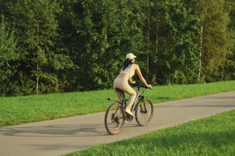 A woman enjoys a leisurely ride on a bicycle along a quiet pathway surrounded by lush green trees