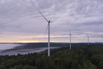 Three wind turbines above a forest at dusk under a cloudy sky, near Schorndorf, Rems-Murr district,