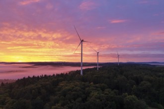 Three wind turbines above a forest in front of sunrise in a vivid colour mood, near Schorndorf,