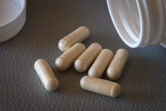 Six beige capsules lie near an open bottle on a dark surface, food supplement, iron supplement,