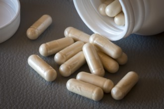 Several beige capsules scattered from an open bottle on a surface, food supplement, iron