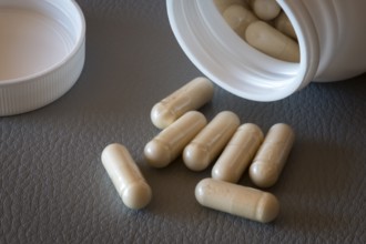 Open bottle with beige capsules and separate lid on one surface, food supplement, iron supplement,