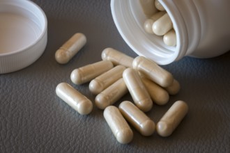 Various beige capsules taken from a half-opened bottle, food supplement, iron supplement, vitamin
