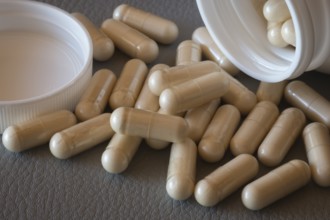 Close-up of beige capsules rolling out of an open bottle onto a surface, food supplement, iron