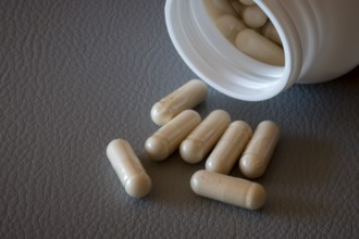 Partially emptied bottle with beige capsules on a textured surface, food supplement, iron