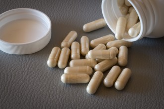 Beige capsules that have fallen from an open bottle with the lid removed onto a surface, food