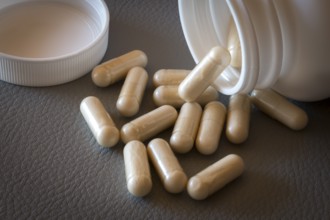 Beige capsules lying on a textured surface from an opened bottle, food supplement, iron supplement,