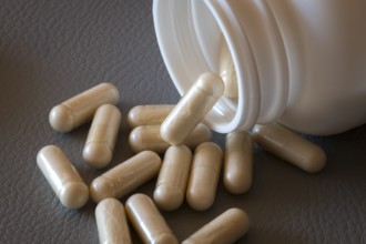 Beige capsules roll out of an open bottle onto a dark surface, food supplement, iron supplement,