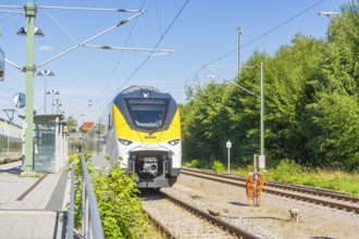Train travelling under a blue sky on tracks past trees and signals, battery Electric train with